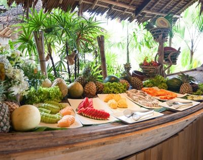 A tropical buffet with an array of fruits under a thatched roof.