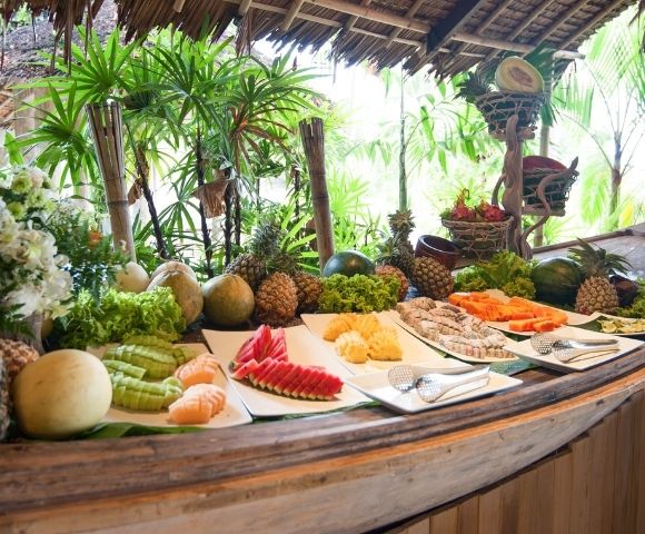 A tropical buffet with an array of fruits under a thatched roof.