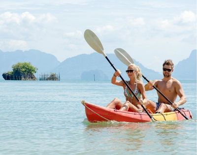 Two people kayaking in calm blue waters with distant mountains.