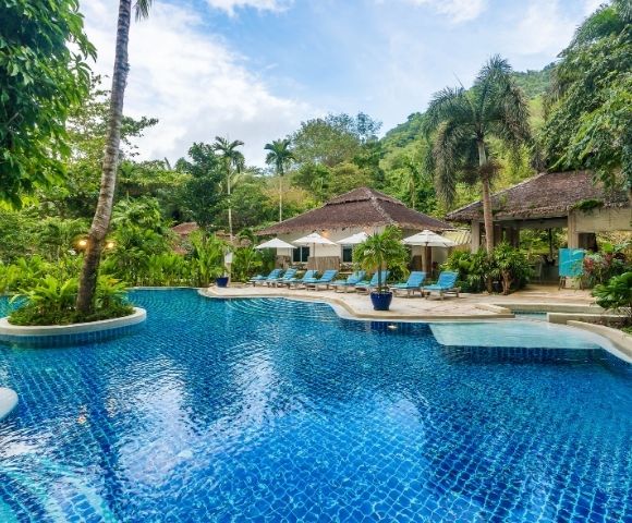 Tropical resort pool with blue water, sun loungers, and lush greenery.