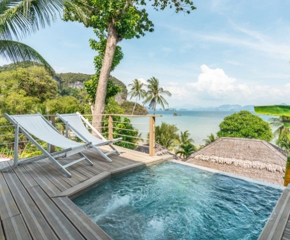 A tropical resort view with an infinity pool, sun loungers, and the ocean in the background.