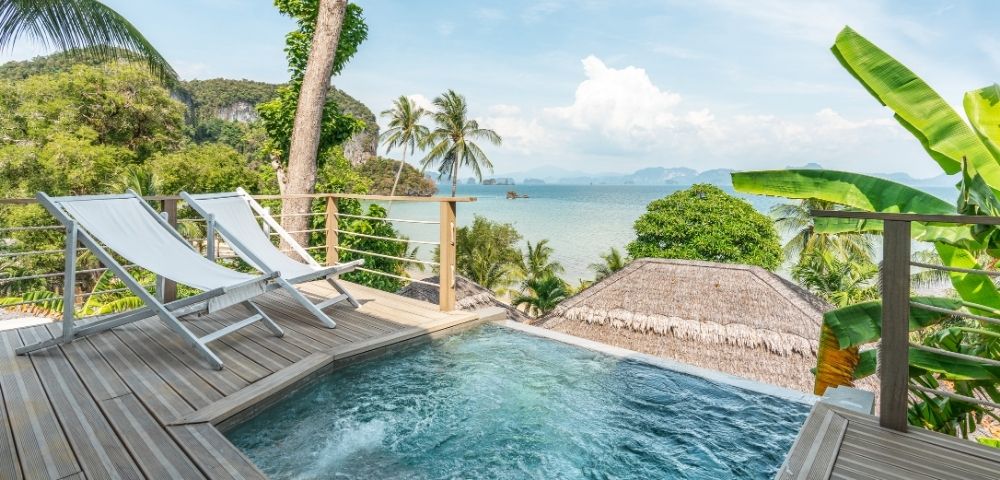 A tropical resort view with an infinity pool, sun loungers, and the ocean in the background.