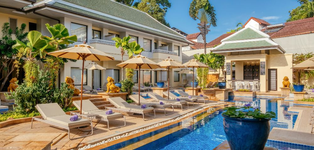 Luxurious hotel pool with loungers and umbrellas, traditional architecture, and tropical plants.