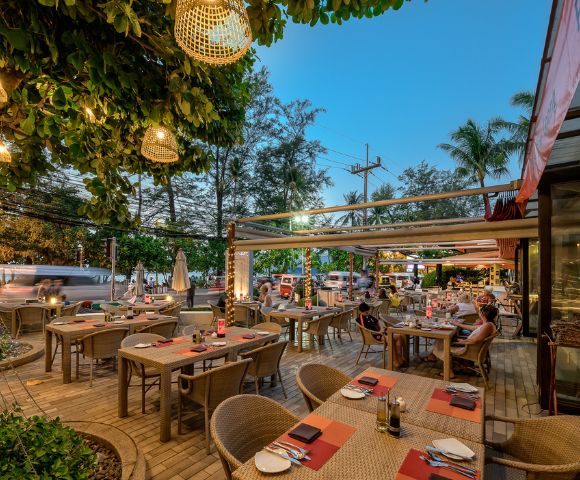 Outdoor restaurant patio with tables set for dining, string lights, and evening ambiance.