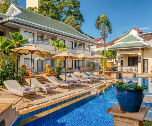 Luxurious hotel pool with loungers and umbrellas, traditional architecture, and tropical plants.