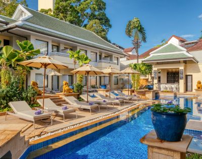 Luxurious hotel pool with loungers and umbrellas, traditional architecture, and tropical plants.