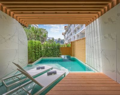 Modern outdoor patio with a pool, wooden deck, loungers, and greenery under a pergola.