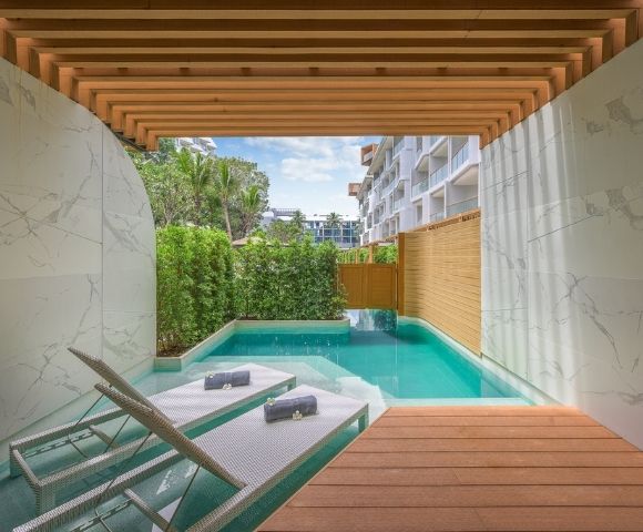 Modern outdoor patio with a pool, wooden deck, loungers, and greenery under a pergola.