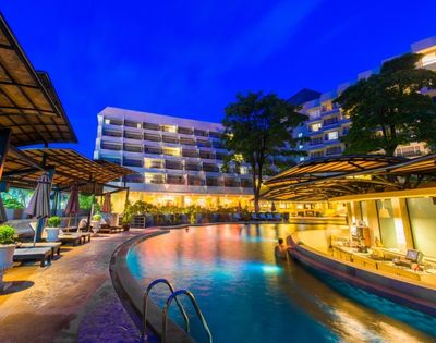 Illuminated resort pool at twilight with buildings in the background.