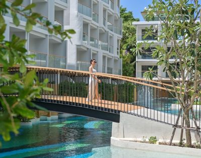A person standing on a bridge over a pool at a modern resort.