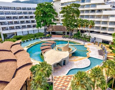 Aerial view of a resort pool area with palm trees and surrounding hotel buildings.