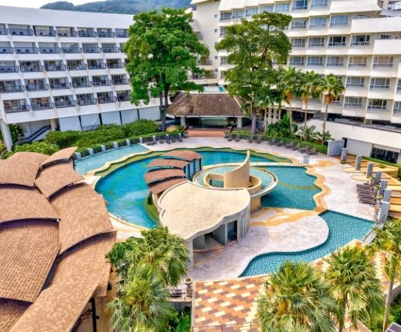 Aerial view of a resort pool area with palm trees and surrounding hotel buildings.