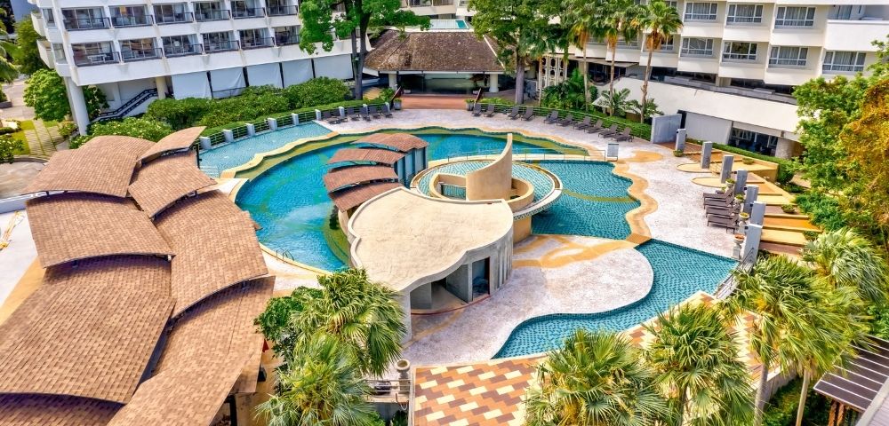 Aerial view of a resort pool area with palm trees and surrounding hotel buildings.