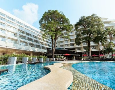 A resort pool with blue mosaic tiles, surrounded by white buildings with balconies and trees.