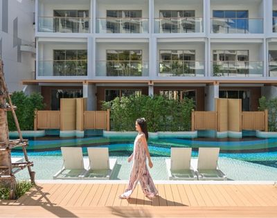 Woman walking by a pool in front of a modern hotel building with loungers and palm trees.