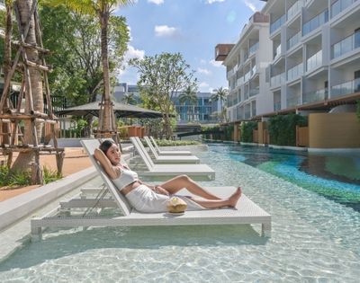 Woman relaxing on a sun lounger in a pool area at a resort.
