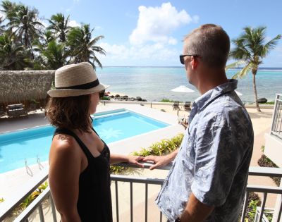 A couple overlooking a pool and beach from a balcony.