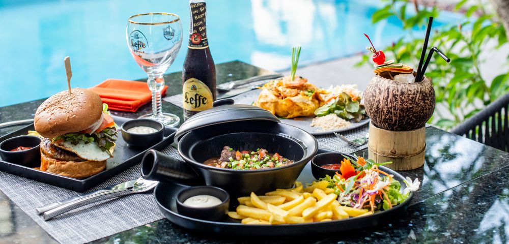 A variety of dishes and a bottle of Leffe beer by a poolside.