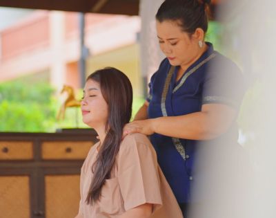 A woman in a blue dress giving a neck massage to a person in a beige top.