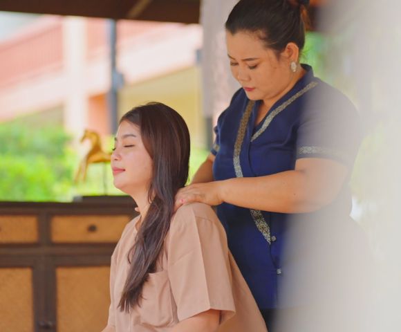 A woman in a blue dress giving a neck massage to a person in a beige top.
