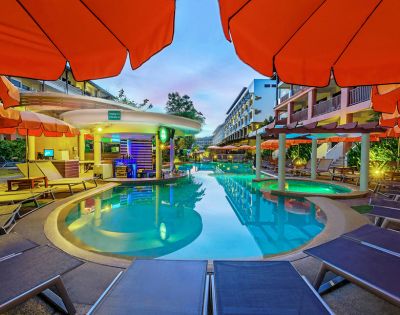 Twilight view of a hotel pool area with surrounding loungers and vibrant orange umbrellas.
