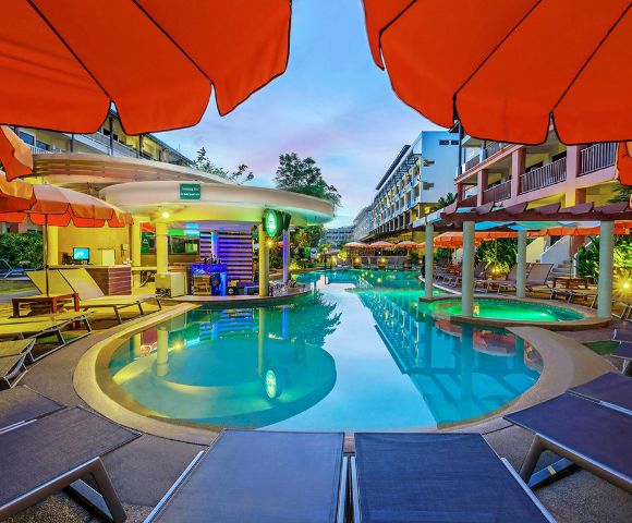 Twilight view of a hotel pool area with surrounding loungers and vibrant orange umbrellas.