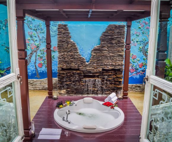 Tranquil spa retreat featuring a jacuzzi surrounded by a stone wall, colorful mural, and lush greenery, perfect for relaxation.