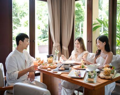 A group enjoying a meal at a beautifully set table surrounded by lush greenery and natural light.