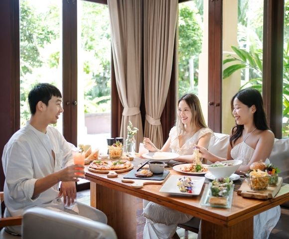 A group enjoying a meal at a beautifully set table surrounded by lush greenery and natural light.