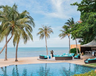 A tranquil beachside resort scene with palm trees, a blue pool, and outdoor seating facing the ocean, creating a serene atmosphere.