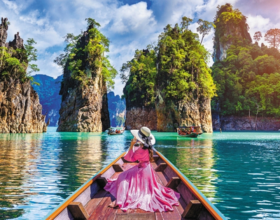 A woman in a pink dress and wide-brimmed hat relaxes on a boat, surrounded by lush islands and turquoise waters.