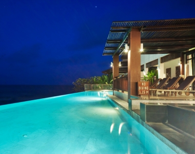 A serene infinity pool at night, illuminated by soft lights, overlooks a calm ocean under a deep blue sky.