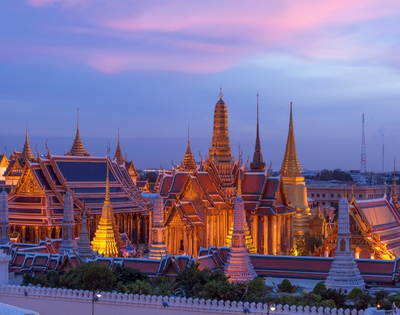Twilight view of Bangkok's Grand Palace, showcasing golden spires and intricate architecture under a colorful sky.