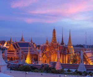 Twilight view of Bangkok's Grand Palace, showcasing golden spires and intricate architecture under a colorful sky.