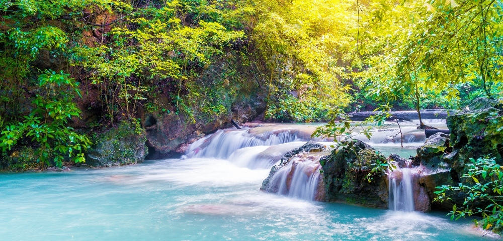 A serene turquoise waterfall surrounded by lush green foliage, creating a peaceful natural oasis.