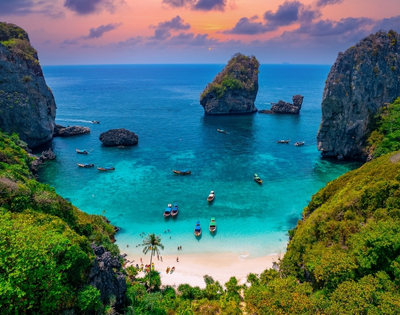 A serene beach cove with turquoise waters, surrounded by rocky cliffs and lush greenery, under a colorful sunset sky.