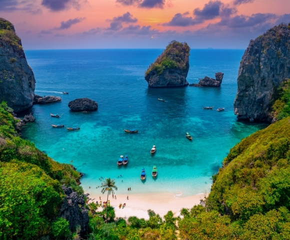 A serene beach cove with turquoise waters, surrounded by rocky cliffs and lush greenery, under a colorful sunset sky.