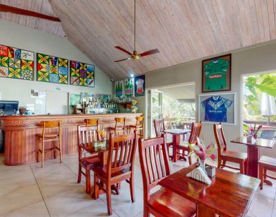Cozy restaurant interior with wooden tables, a bar, vibrant artwork, and jerseys on display under a high, wooden ceiling.