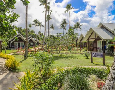 Tropical resort setting with palm trees, lush gardens, and modern bungalows under a partly cloudy sky. Peaceful and inviting atmosphere.