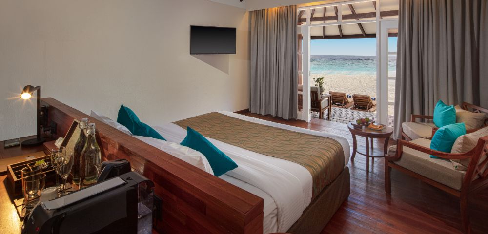 A modern hotel room with a king bed, ocean view, and elegant decor, featuring a TV, lounge chairs, and a cozy seating area.