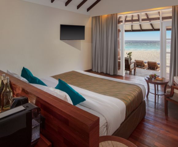 A modern hotel room with a king bed, ocean view, and elegant decor, featuring a TV, lounge chairs, and a cozy seating area.