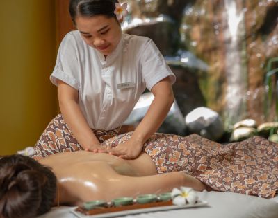 A massage therapist applies oil to a client's back in a serene spa setting, surrounded by lush greenery and a gentle waterfall.