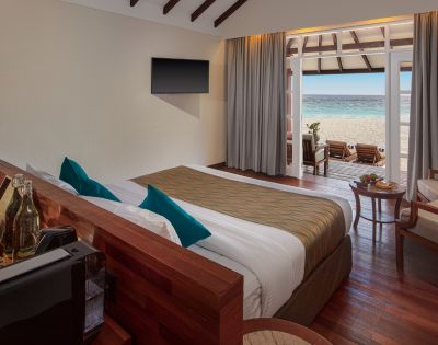 A modern hotel room with a king bed, ocean view, and elegant decor, featuring a TV, lounge chairs, and a cozy seating area.