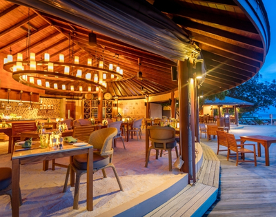 A beautifully designed beachfront restaurant with warm lighting, wooden furniture, and a circular layout, set against a twilight sky.