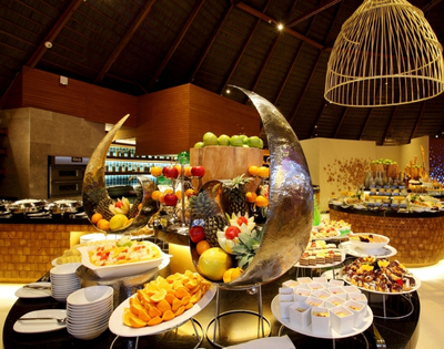 A lavish buffet featuring an array of colorful fruits, desserts, and decorative platters in an elegantly designed dining room.
