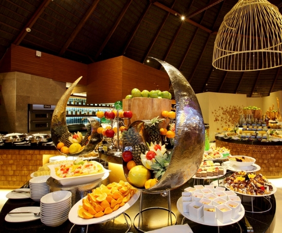 A lavish buffet featuring an array of colorful fruits, desserts, and decorative platters in an elegantly designed dining room.