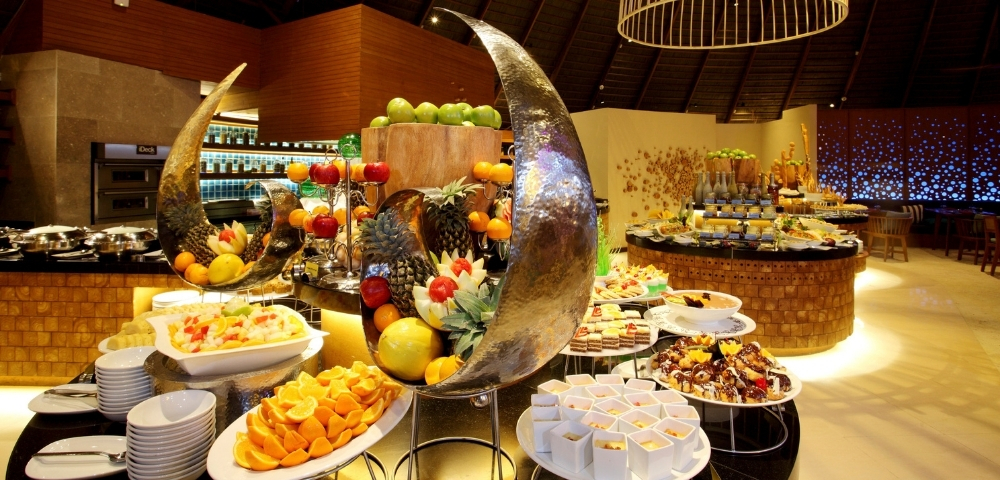 A lavish buffet featuring an array of colorful fruits, desserts, and decorative platters in an elegantly designed dining room.