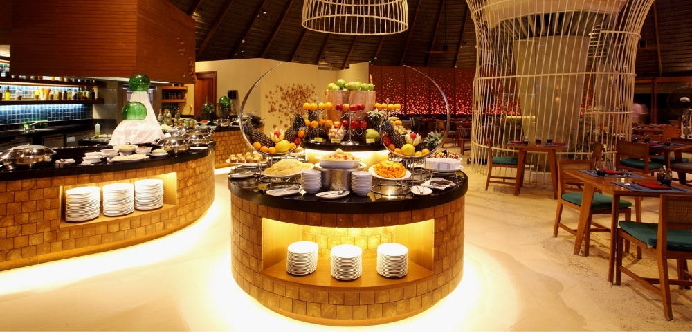 A chic restaurant interior featuring elegantly arranged food displays, colorful fruit, and a striking modern decor with high ceilings.