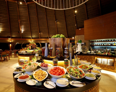 A vibrant buffet displays an array of fresh salads, sauces, and fruits in a tropical restaurant setting with wooden decor.