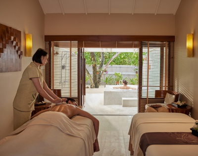 A serene spa room with a therapist giving a massage to a client, while another person enjoys a relaxing soak in a private outdoor tub.